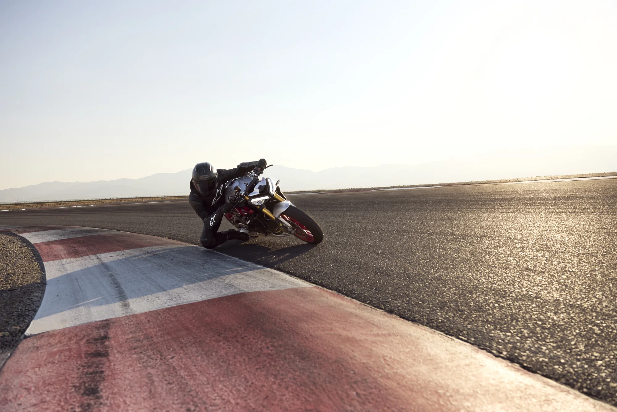 Street Triple 765 RX inclinada al trazar una curva de circuito, vista a distancia sobre el piano rojo y blanco