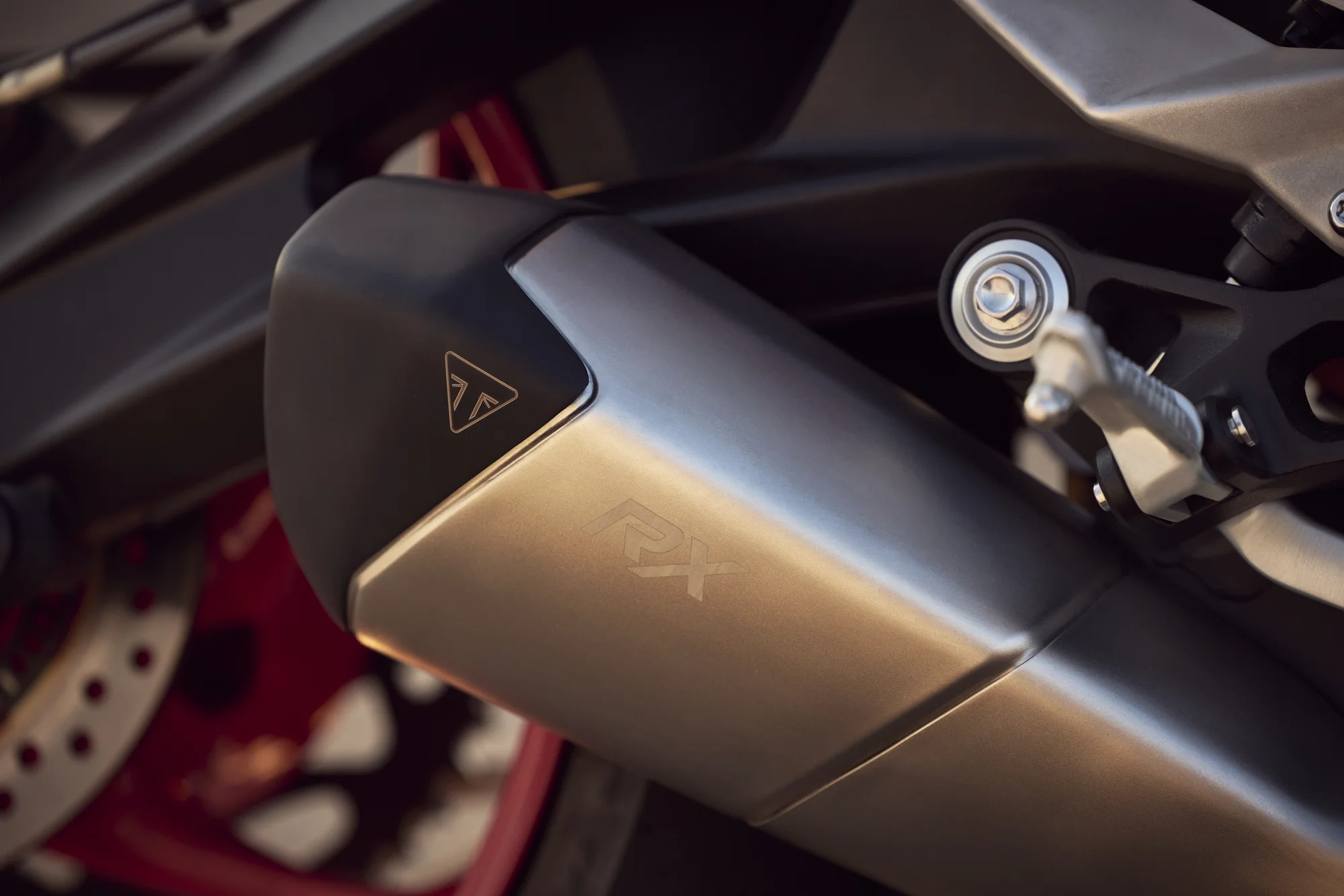 Silenciador lateral de la Street Triple 765 RX con el logo RX grabado, junto al disco de freno y la llanta Diablo Red