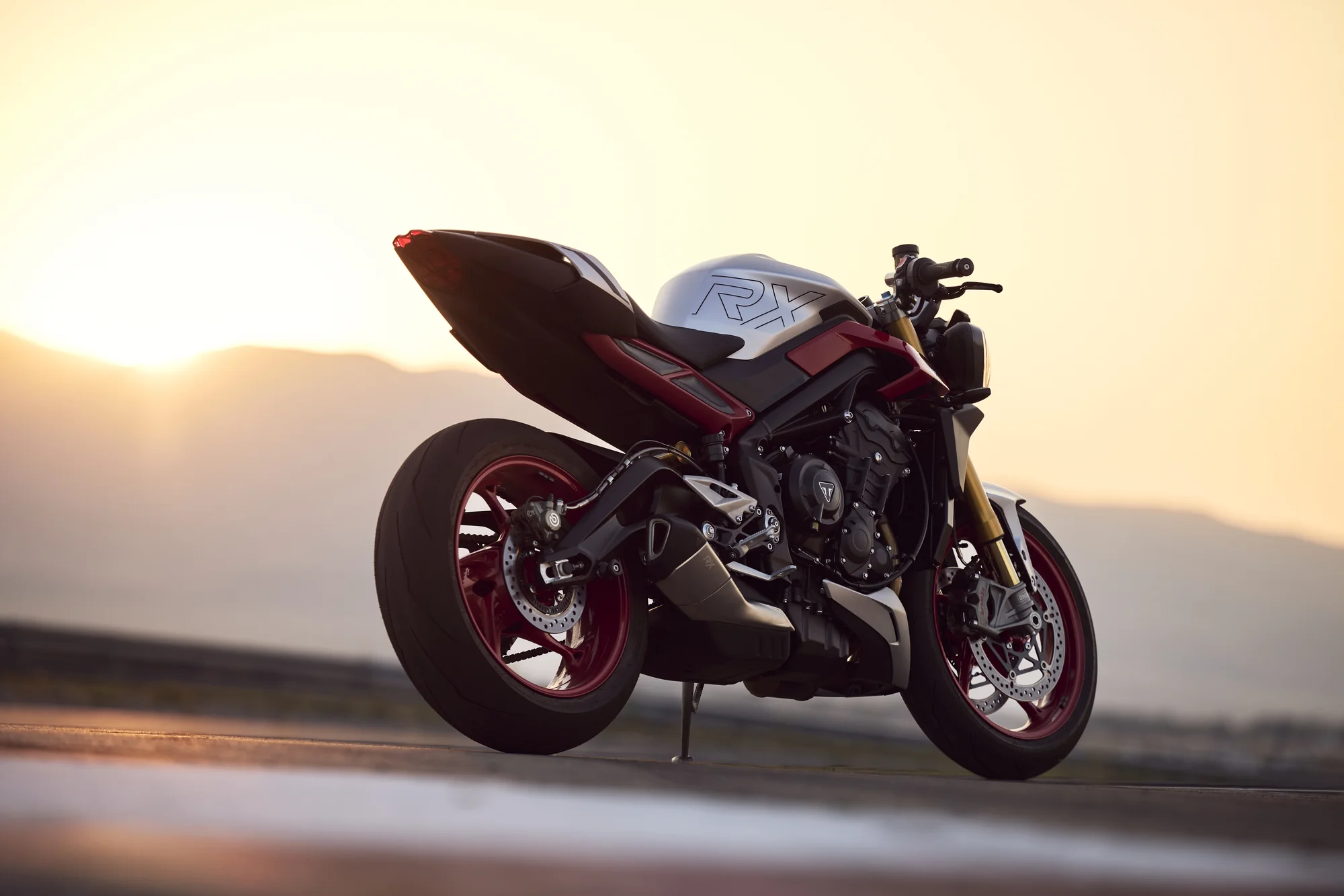 Street Triple 765 RX en tres cuartos trasero a contraluz al atardecer, con el logo RX en el colín