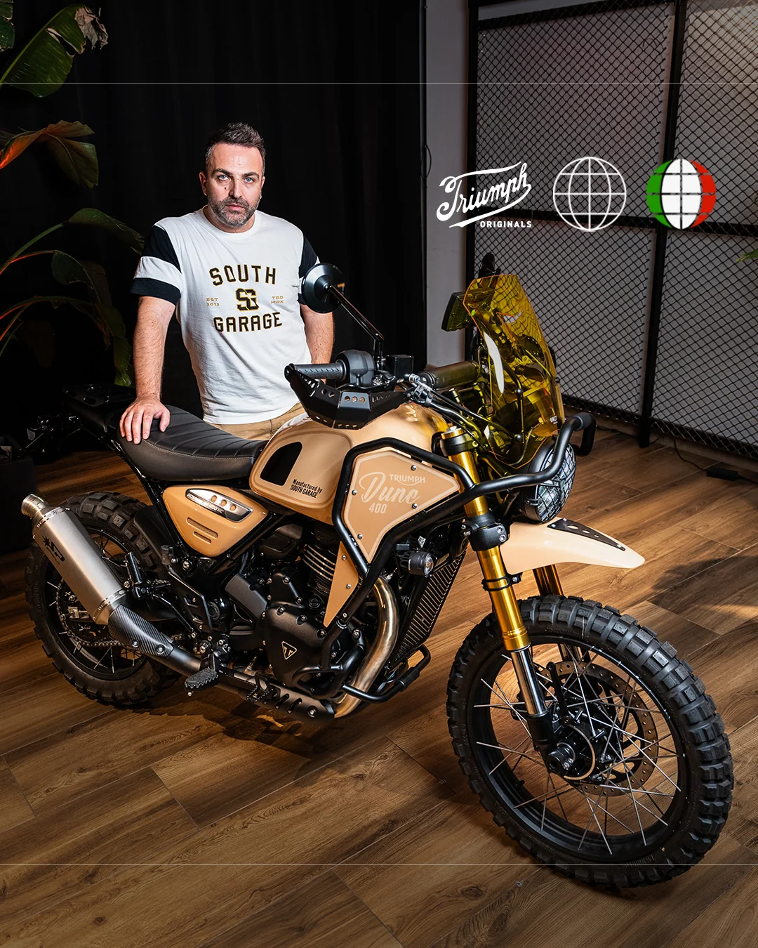 Dune 400 de South Garage: Scrambler color arena con parabrisas amarillo, junto a un hombre con camiseta del taller