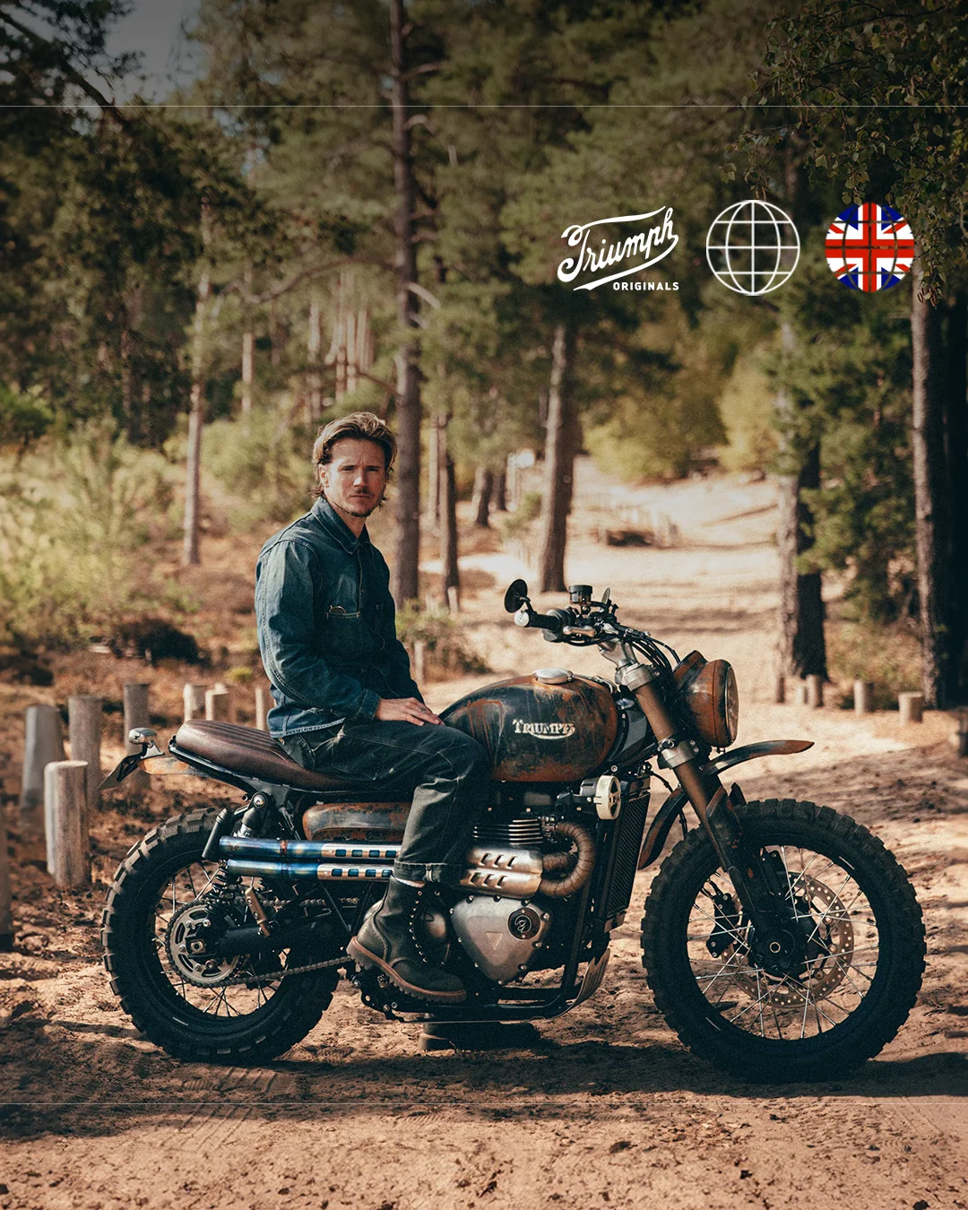 Scrambler 900 de Stockwell Design con acabado envejecido, con su piloto sentado en un camino de bosque