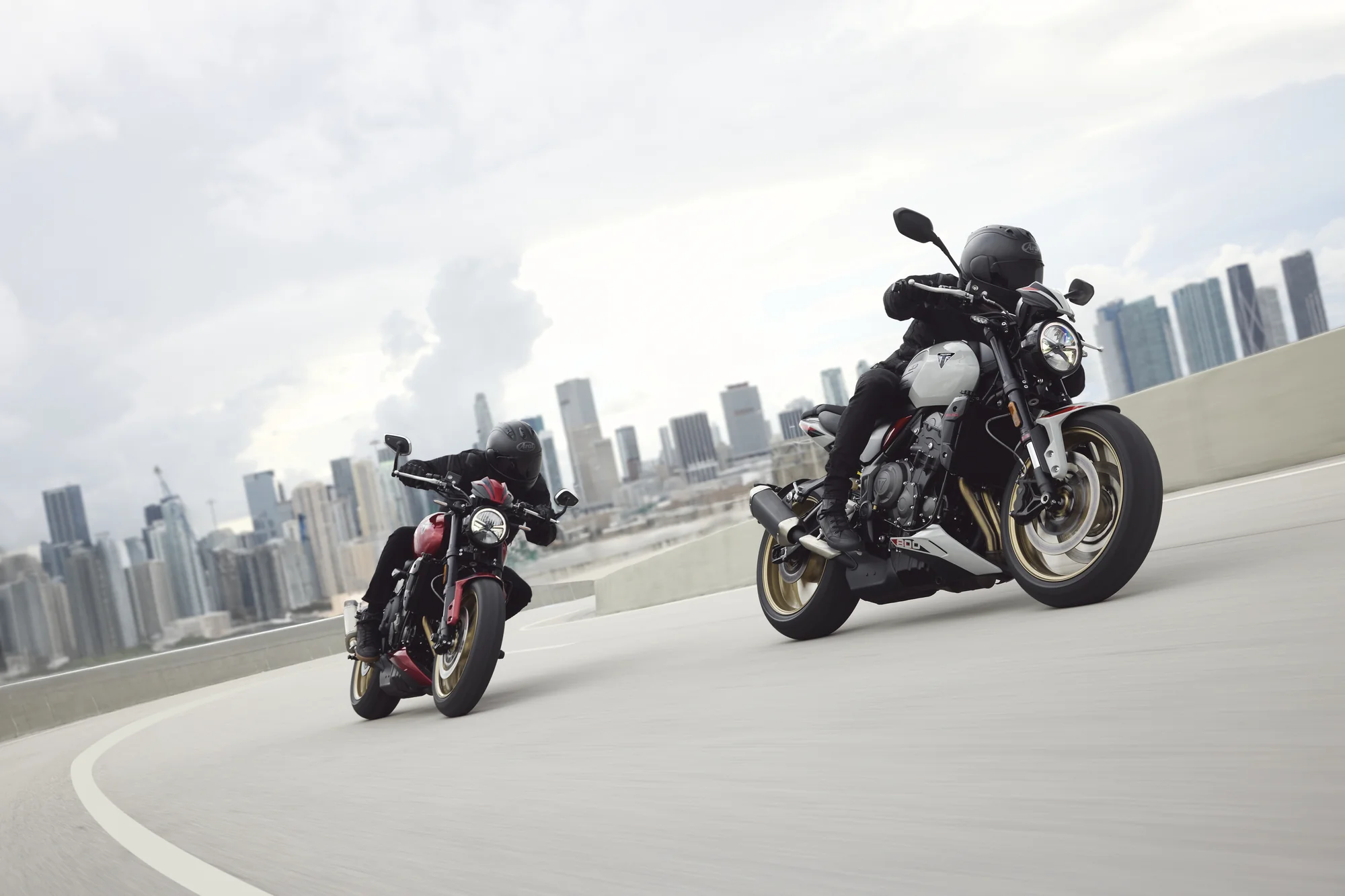 Pilotos en motocicletas Triumph Trident 800 con edificios de la ciudad al fondo