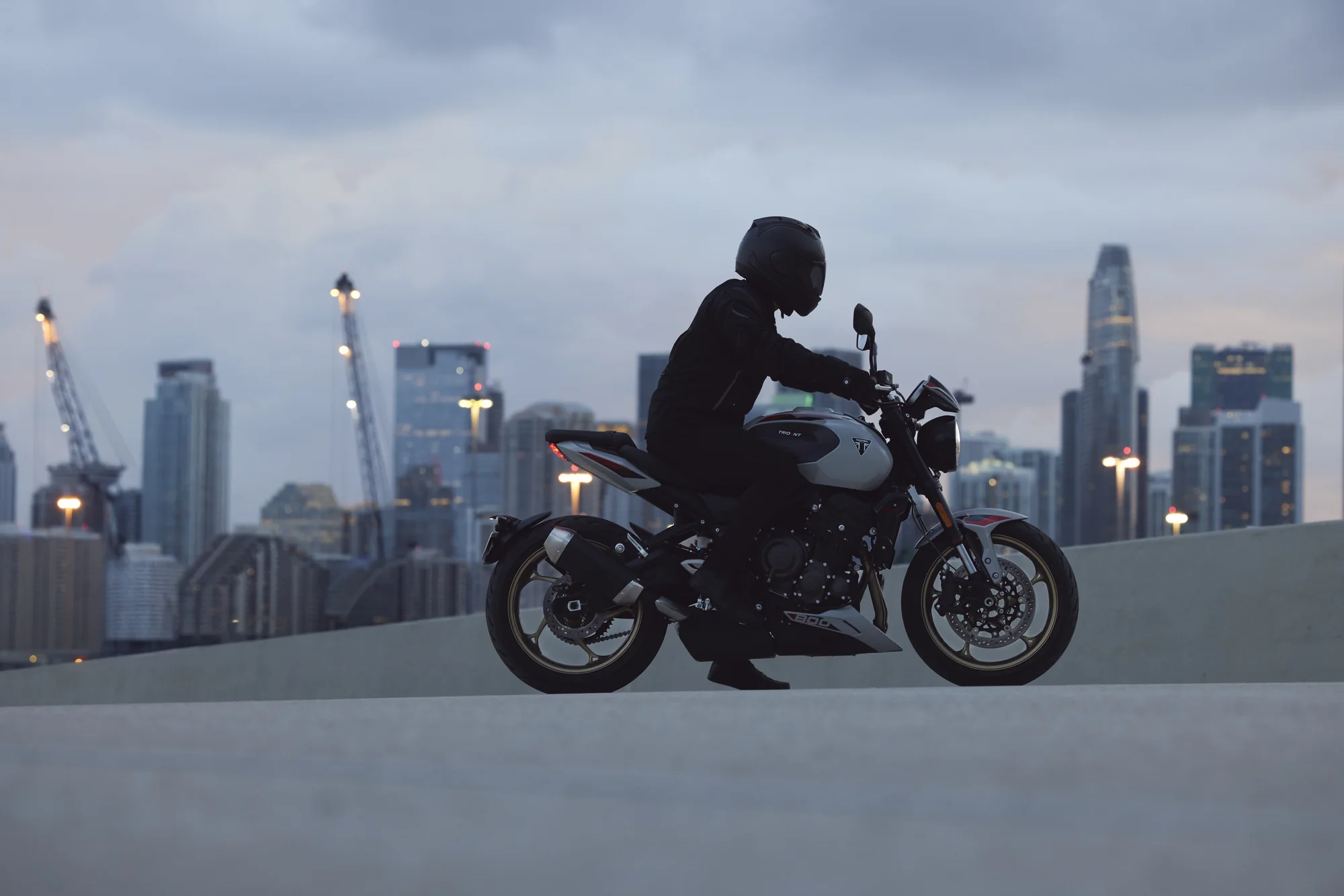 Vista lateral de un piloto sobre la Triumph Trident 800 frente al paisaje urbano
