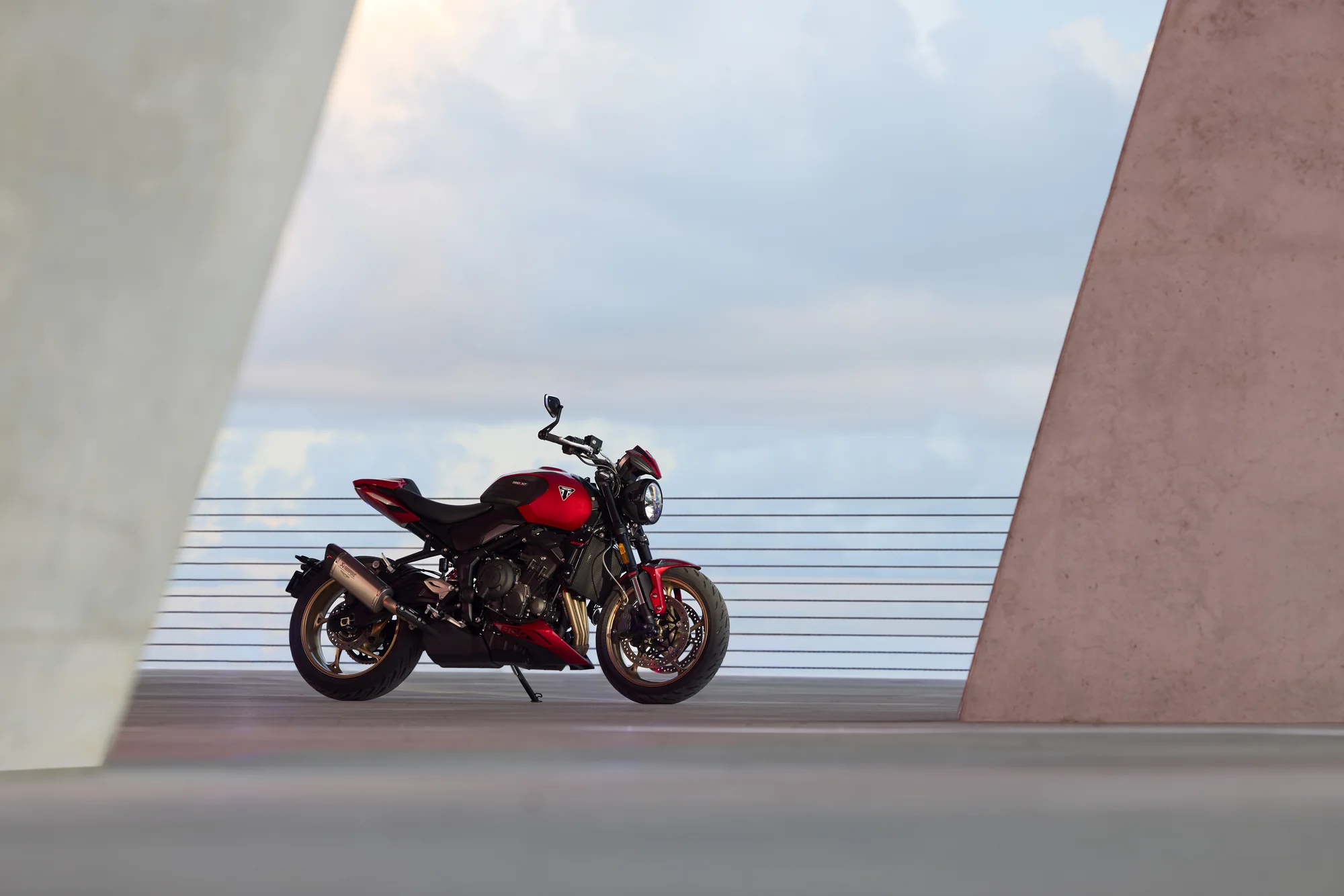 Triumph Trident 800 roja estacionada de perfil junto a una estructura arquitectónica