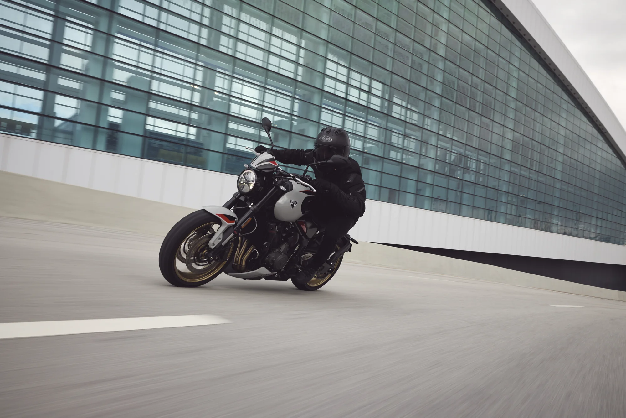 Piloto conduciendo una Triumph Trident 800 junto a un edificio de cristal